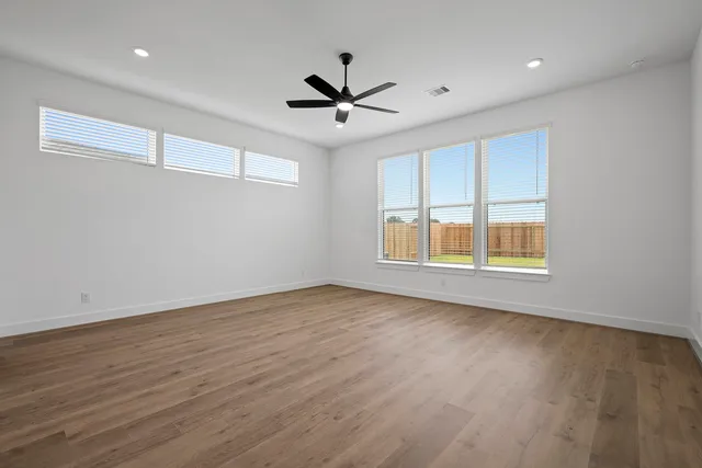 an empty room with wooden floor ceiling fan and windows