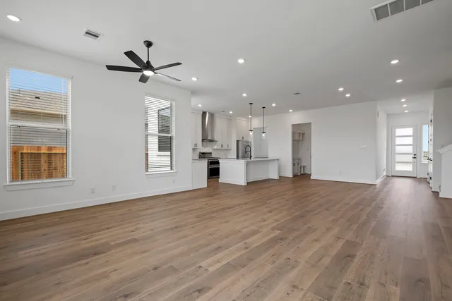 a view of an empty room with wooden floor kitchen view and a window