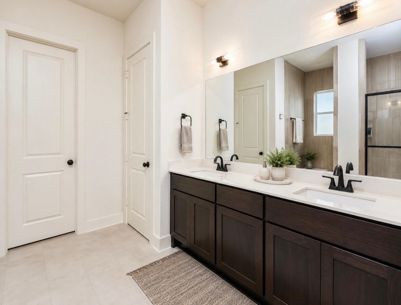 31915 Sky Rdg Lane Fulshear, TX 77441 - Photo 27 of 38 This bathroom features a modern double vanity with dark wood cabinets, large mirror, and sleek black fixtures. It has neutral tile flooring, a spacious layout, and a well-lit atmosphere with contemporary lighting.