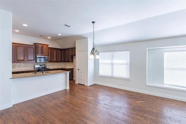 a kitchen with stainless steel appliances granite countertop a refrigerator a sink dishwasher a stove and white countertops with wooden floor