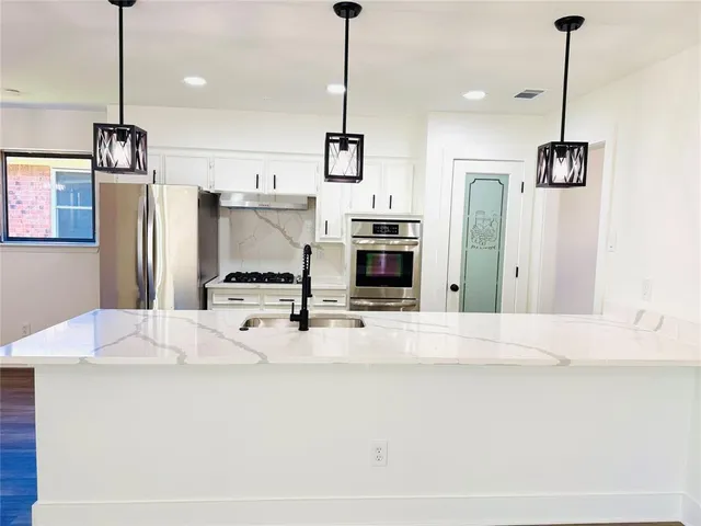 a kitchen with stainless steel appliances kitchen island granite countertop a refrigerator a stove and a sink