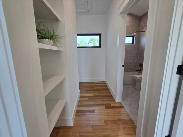 a view of a hallway with wooden floor and a bathroom