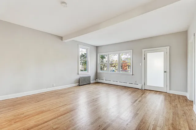 an empty room with wooden floor chandelier and windows
