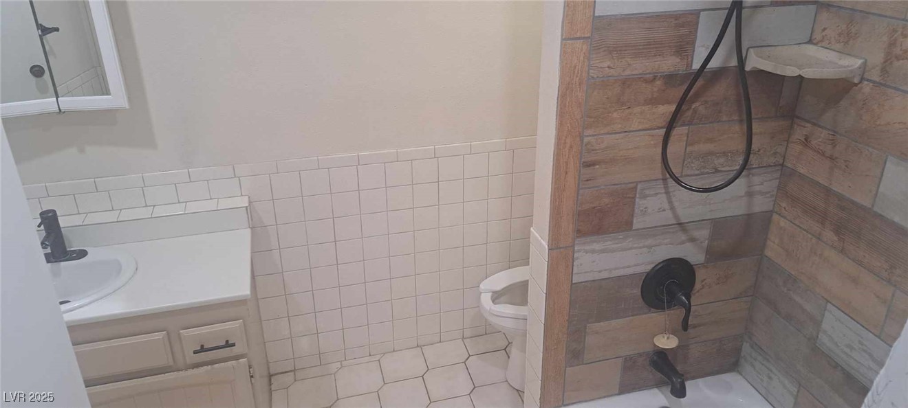 5231 Smoke Ranch Road Las Vegas, NV 89108 - Photo 16 of 23 Full bath featuring wainscoting, toilet, tile patterned flooring, vanity, and tile walls