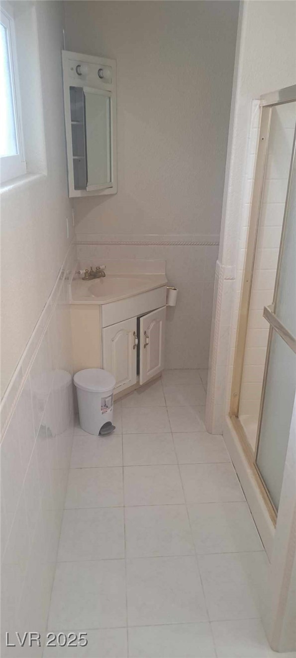 5231 Smoke Ranch Road Las Vegas, NV 89108 - Photo 18 of 23 Full bathroom featuring tile patterned flooring, a wainscoted wall, vanity, tile walls, and a stall shower