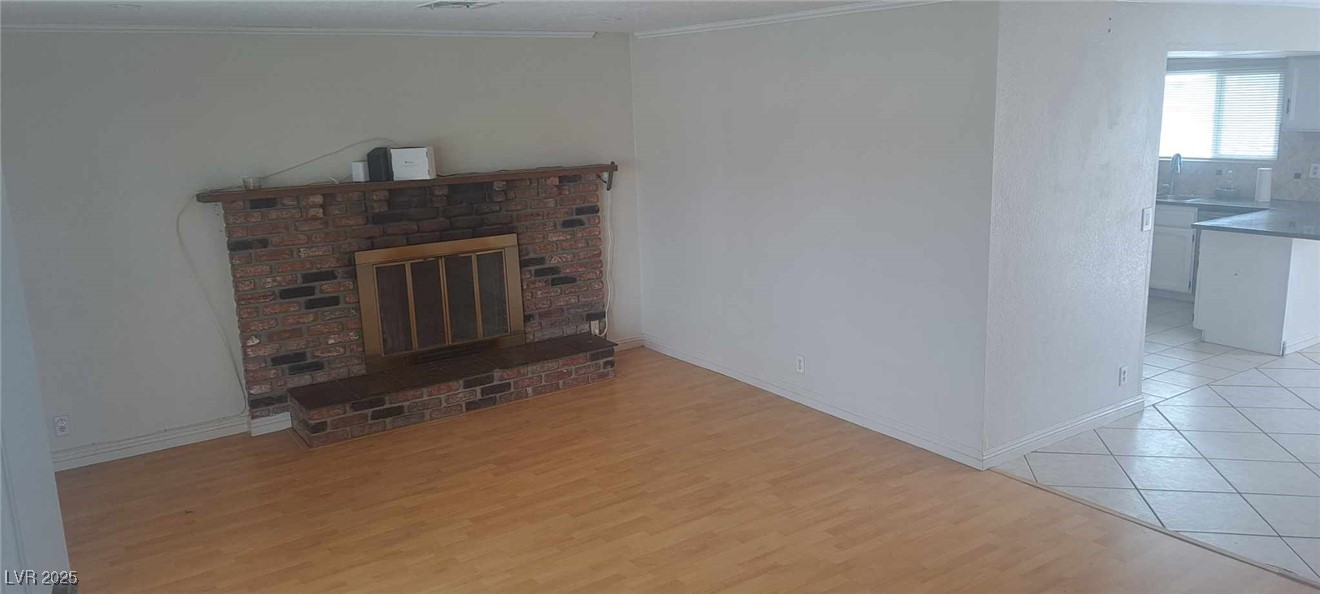 Unfurnished living room with baseboards, light wood finished floors, a brick fireplace, and crown molding