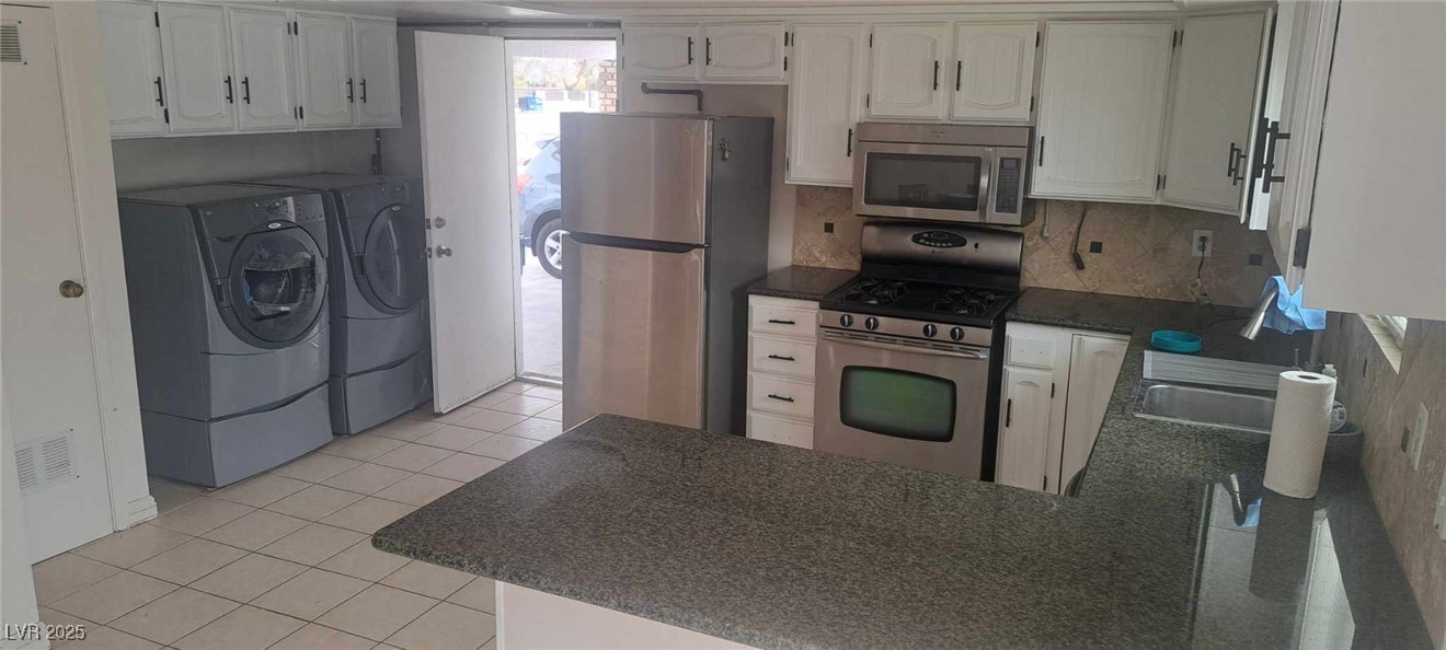 5231 Smoke Ranch Road Las Vegas, NV 89108 - Photo 9 of 23 Kitchen with light tile patterned floors, dark countertops, appliances with stainless steel finishes, washing machine and clothes dryer, and a peninsula