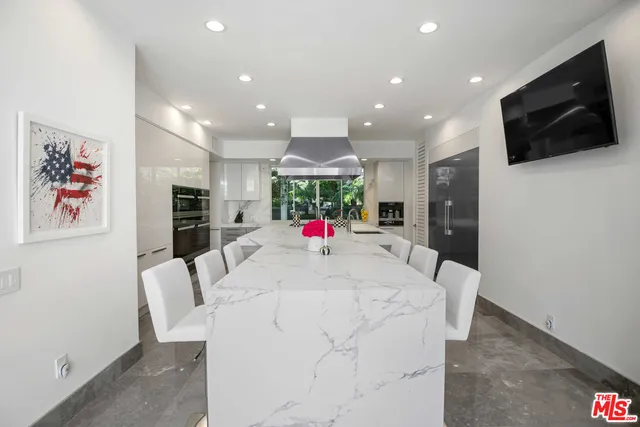 a large white kitchen with stainless steel appliances wooden floor and a flat screen tv