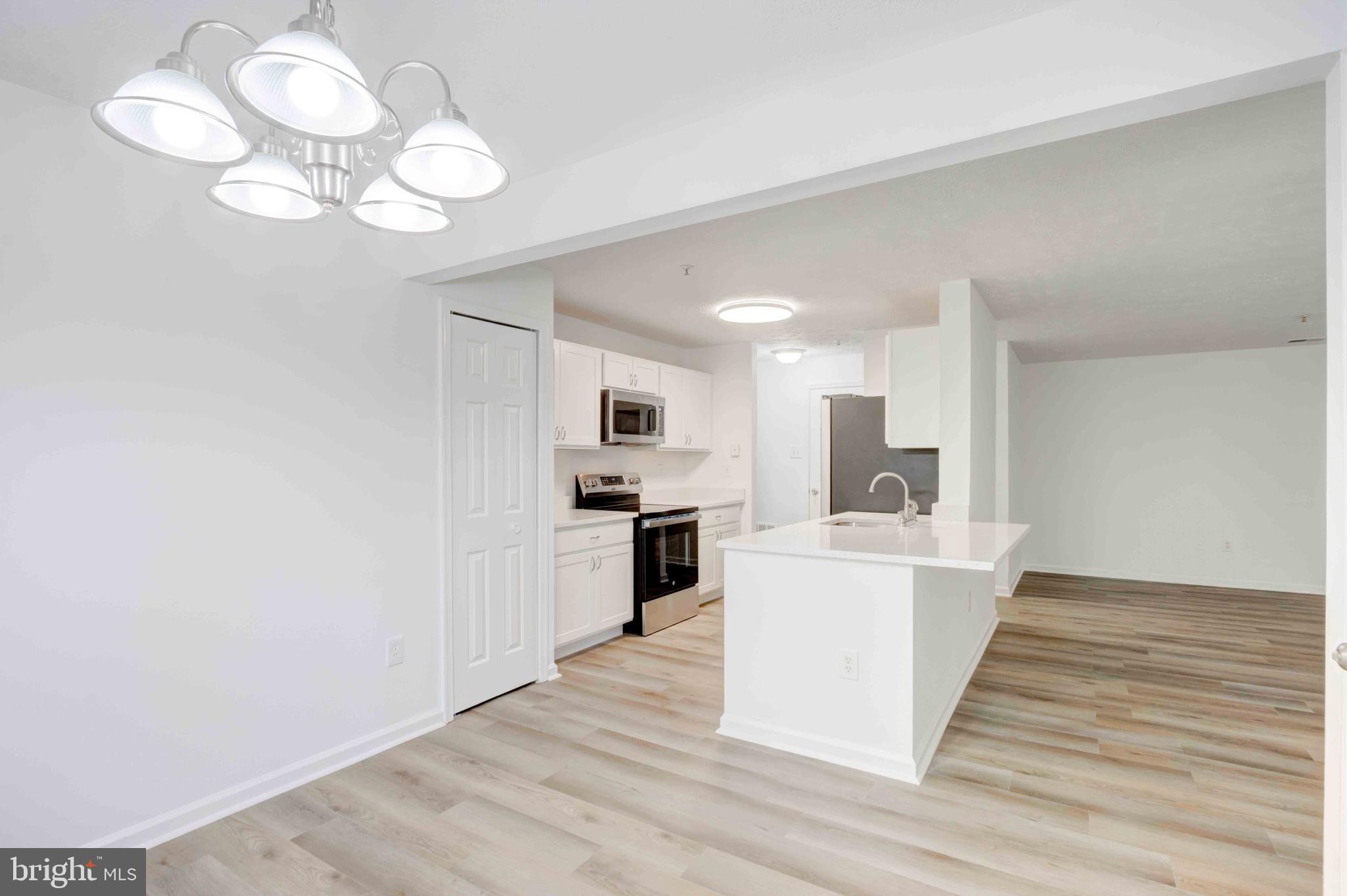 7903 Valley Manor Road, Unit 103 Owings Mills, MD 21117 - Photo 20 of 58 a large white kitchen with kitchen island a stove a sink dishwasher and white cabinets with wooden floor