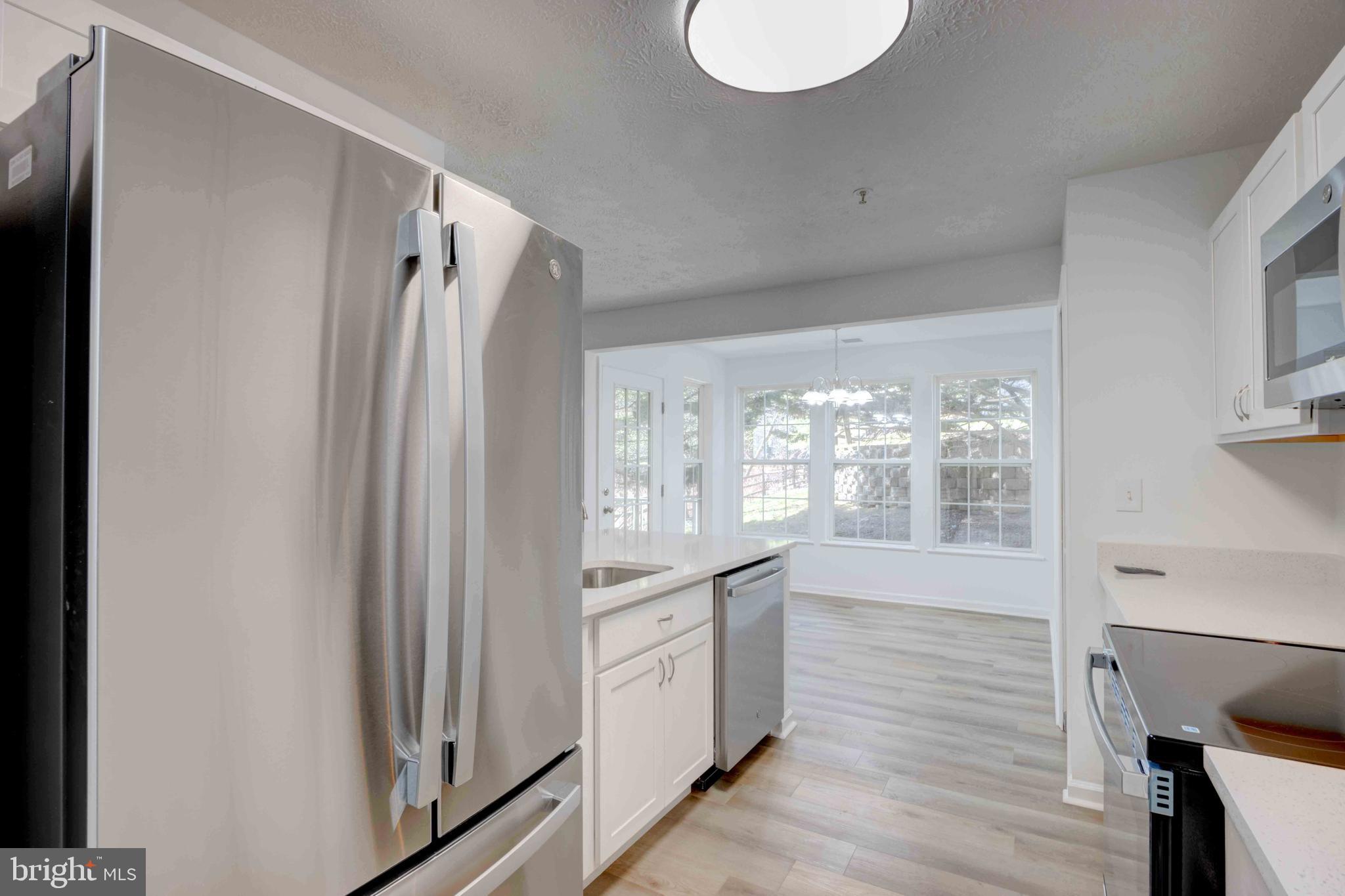 7903 Valley Manor Road, Unit 103 Owings Mills, MD 21117 - Photo 23 of 58 a kitchen with stainless steel appliances granite countertop a refrigerator a sink and white cabinets with wooden floor