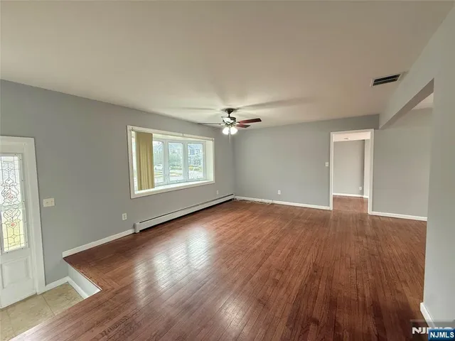 an empty room with wooden floor chandelier fan and windows