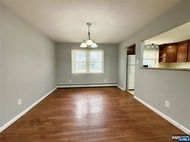 an empty room with wooden floor exposed radiator and windows