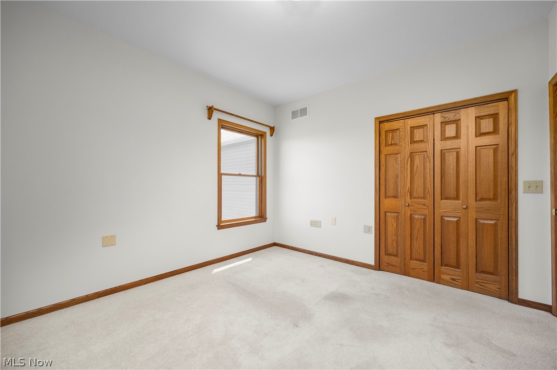 51488 Peck Wadsworth Road Wellington, OH 44090 - Photo 40 of 50 Neutral-toned carpeted room featuring a double-pane window with wood trim, wood baseboards, and a wood bi-fold closet door