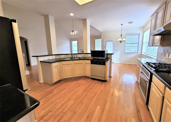a large kitchen with stainless steel appliances a stove a sink dishwasher a refrigerator white cabinets and wooden floor