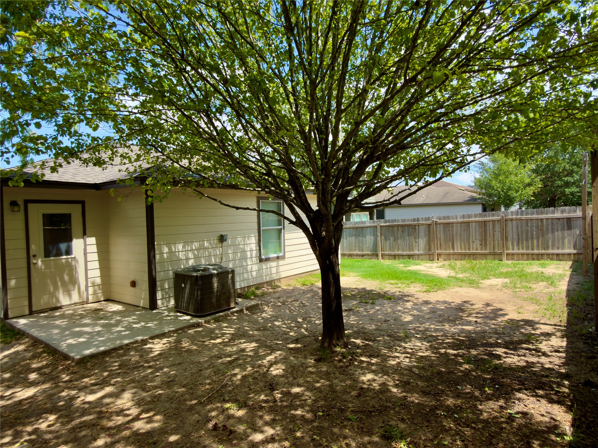 255 Myrtle Street Kyle, TX 78640 - Photo 29 of 31 Spacious backyard featuring a prominent mature tree, concrete patio, tan siding, and a wooden privacy fence