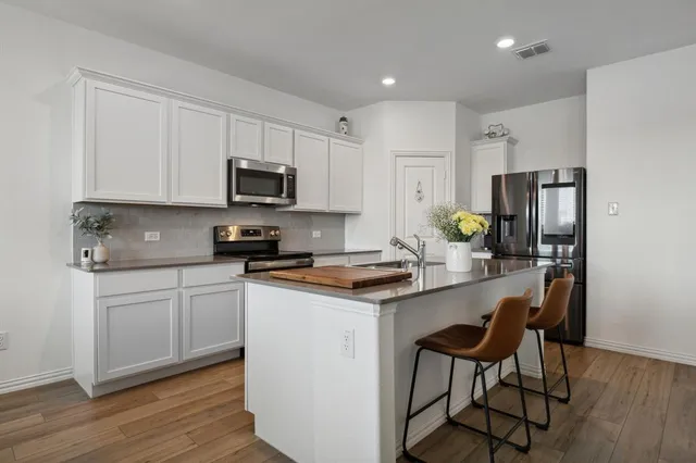 a kitchen with stainless steel appliances granite countertop a stove a sink a refrigerator and white cabinets