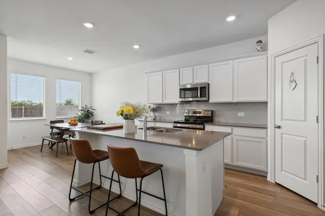 a kitchen with stainless steel appliances granite countertop a stove a sink a microwave a refrigerator and white cabinets with wooden floor