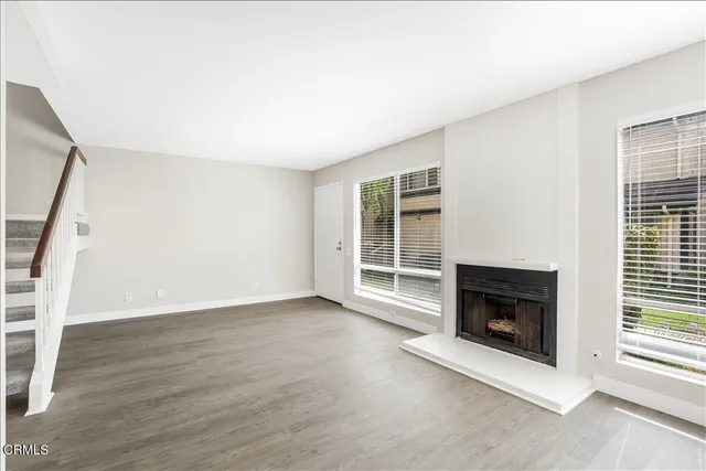 an empty room with wooden floor fireplace and windows
