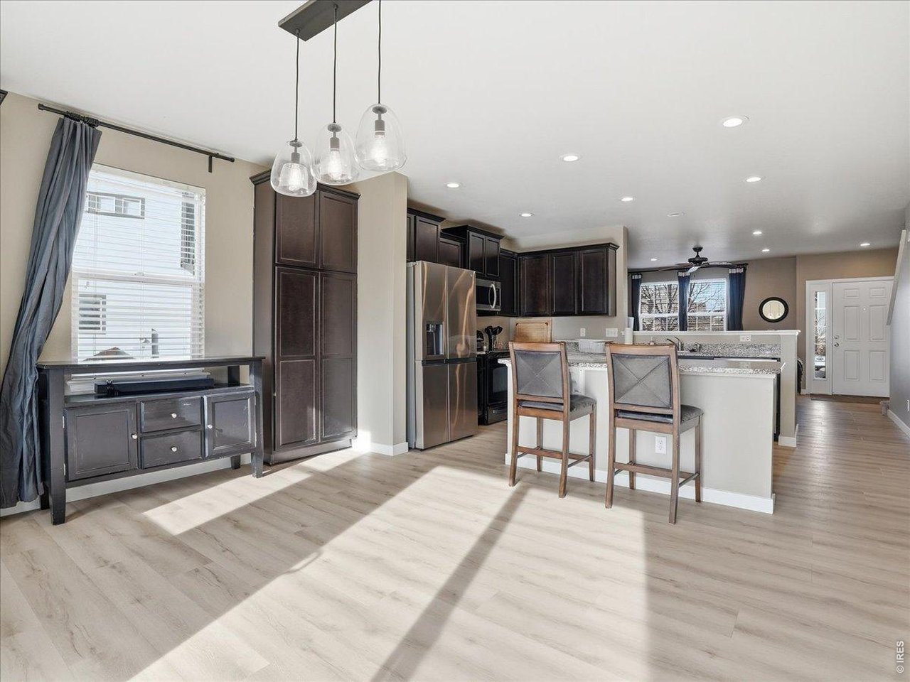 1565 Basildon Court Windsor, CO 80550 - Photo 8 of 36 a living room with stainless steel appliances kitchen island granite countertop a refrigerator a stove top oven and a dining table with wooden floor