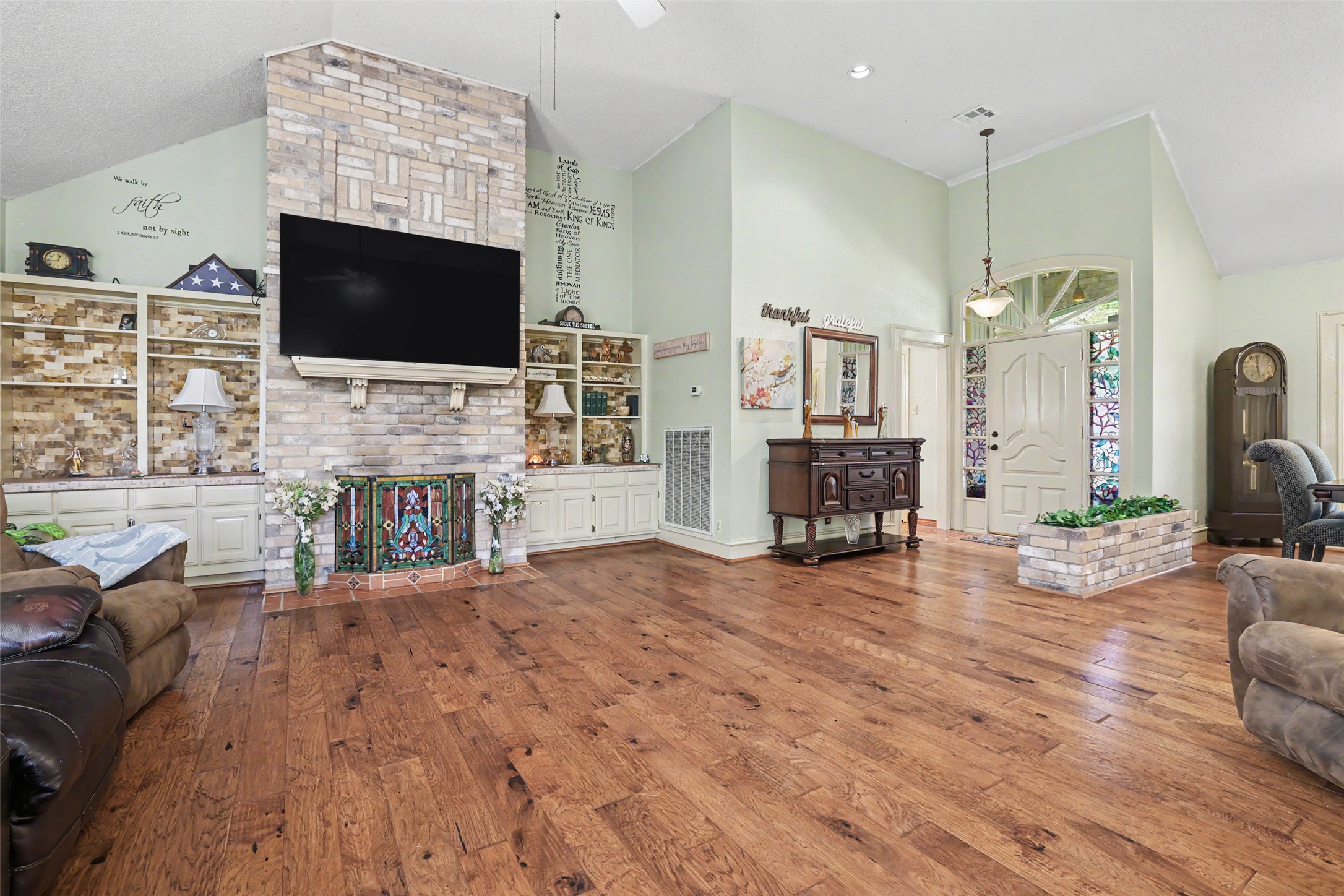 110 South Ridge Circle Georgetown, TX 78628 - Photo 7 of 37 Expansive living area featuring wood-finish flooring, a brick fireplace with built-in shelving, vaulted ceilings, and an arched entry door with decorative glass