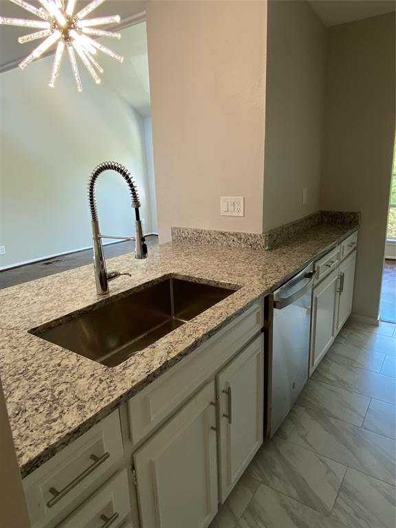 3936 Travis Street Dallas, TX 75204 - Photo 12 of 17 Kitchen island featuring a stainless steel sink with a high-arc faucet, granite countertops, white cabinetry with silver hardware, and a stainless steel dishwasher