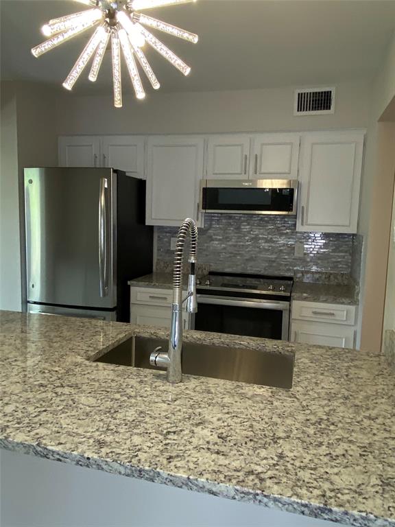 3936 Travis Street Dallas, TX 75204 - Photo 13 of 17 Kitchen featuring a contemporary chandelier, stainless steel appliances, white cabinetry, a mosaic tile backsplash, and light-toned stone countertops with an undermount sink