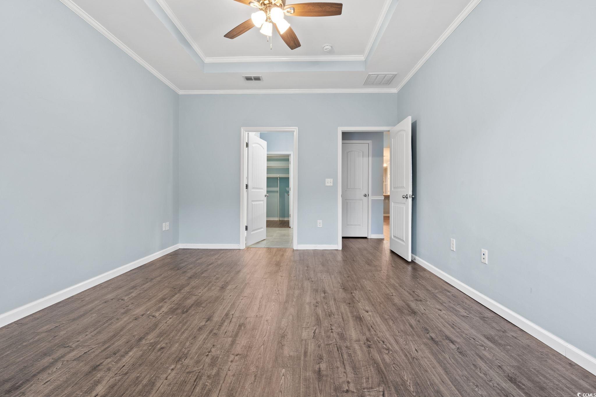 797 Salerno Circle, Unit C Myrtle Beach, SC 29579 - Photo 13 of 40 Unfurnished bedroom with a raised ceiling, a spacious closet, dark wood-style flooring, a ceiling fan, and crown molding