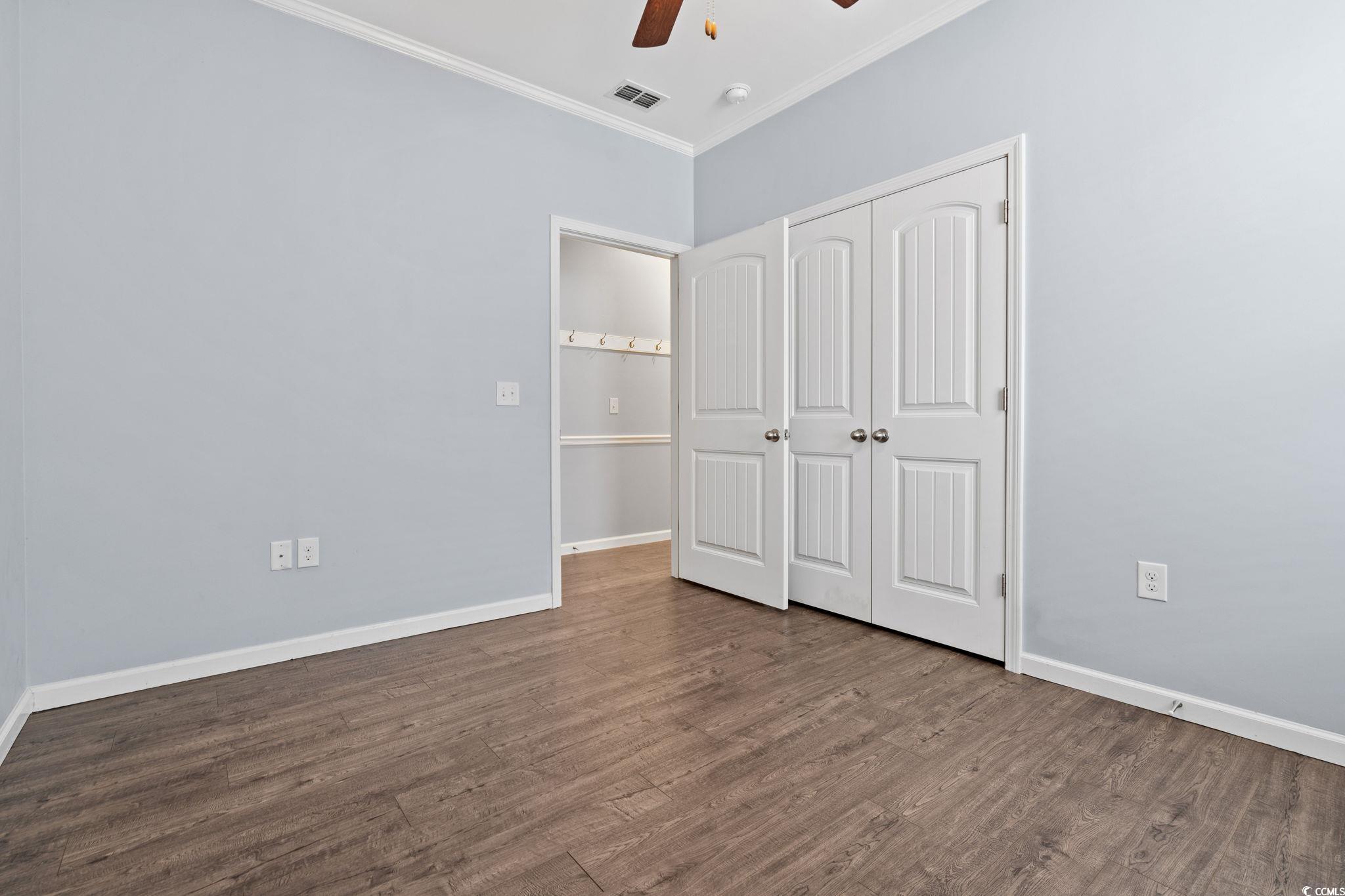 797 Salerno Circle, Unit C Myrtle Beach, SC 29579 - Photo 27 of 40 Unfurnished bedroom featuring ornamental molding, dark wood-style floors, a ceiling fan, and a closet