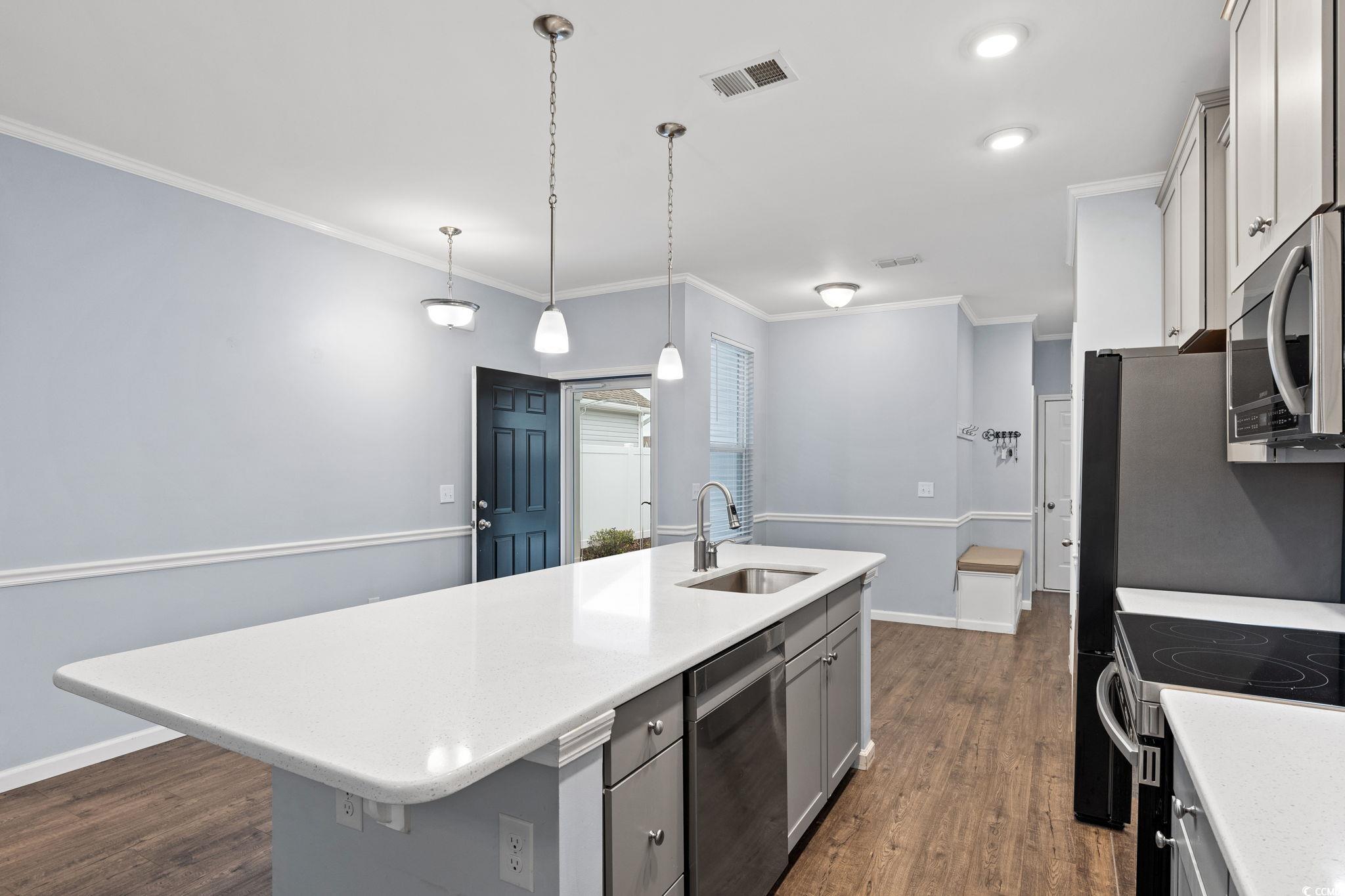 797 Salerno Circle, Unit C Myrtle Beach, SC 29579 - Photo 6 of 40 Kitchen featuring a center island with sink, gray cabinetry, dark wood-style flooring, stainless steel appliances, and ornamental molding