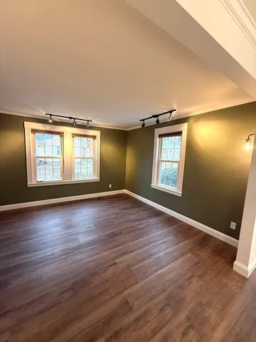 an empty room with wooden floor and windows with curtains