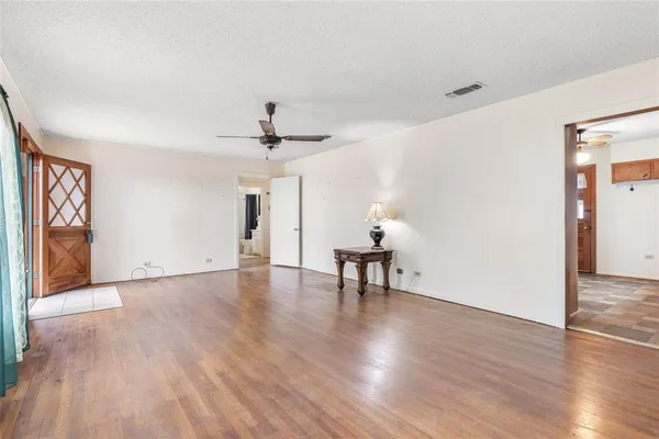a view of an empty room with wooden floor and a ceiling fan