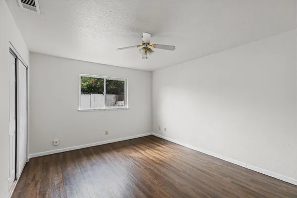 an empty room with wooden floor chandelier fan and windows