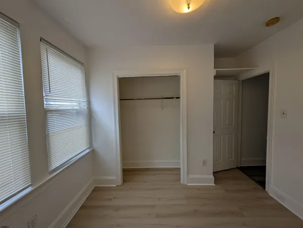 an empty room with wooden floor closet and windows