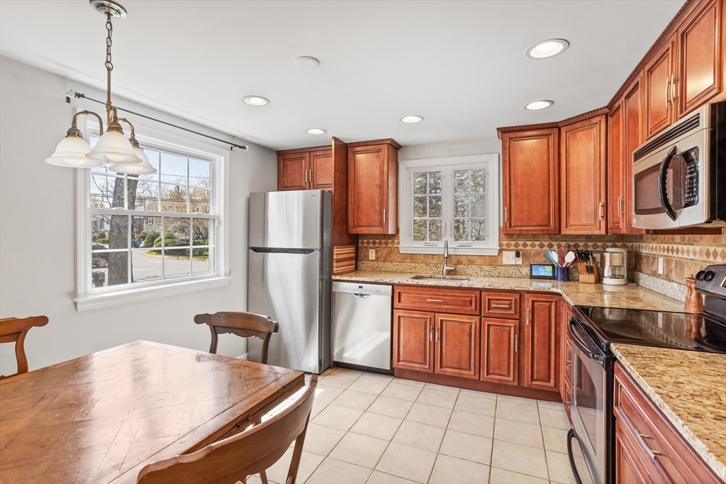 66 Old Stow Road Concord, MA 01742 - Photo 11 of 42 a kitchen with stainless steel appliances granite countertop a stove top oven a sink dishwasher a dining table and chairs with wooden floor