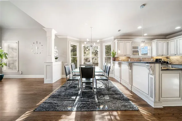 a kitchen with stainless steel appliances kitchen island granite countertop a stove a refrigerator a dining table and chairs with wooden floor