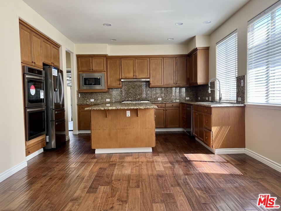 26526 Beecher Lane Stevenson Ranch, CA 91381 - Photo 7 of 31 a kitchen with stainless steel appliances granite countertop a refrigerator a stove top oven a sink and dishwasher with wooden floor