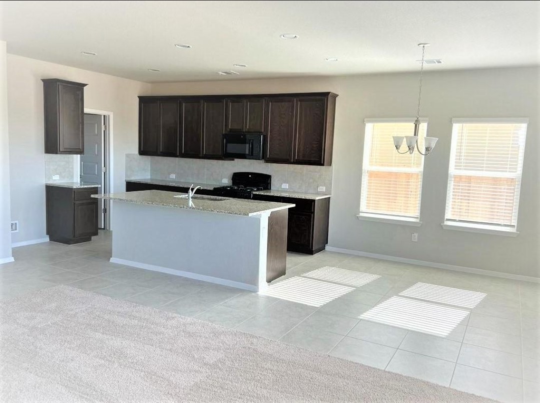 2771 Winding Creek Road Kyle, TX 78640 - Photo 5 of 24 Granite counters and dark wood cabinets define this bright, open-concept kitchen with tile and carpeted floors.