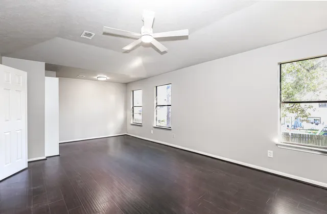 an empty room with wooden floor fan and windows