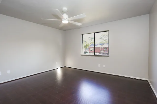 an empty room with wooden floor fan and windows