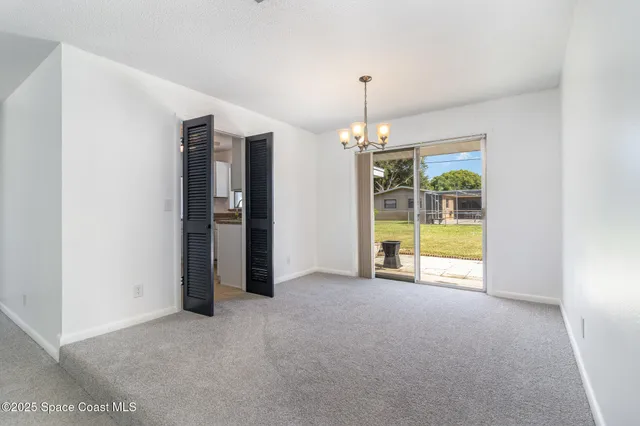 a view of an empty room with chandelier fan and kitchen view