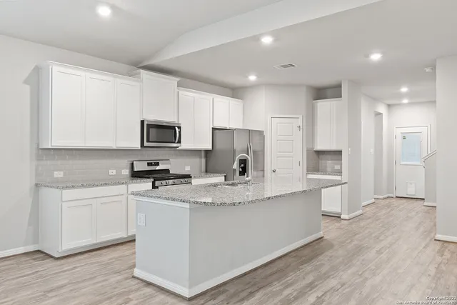 a kitchen with stainless steel appliances granite countertop a sink a stove a refrigerator a microwave oven with white cabinets and wooden floor