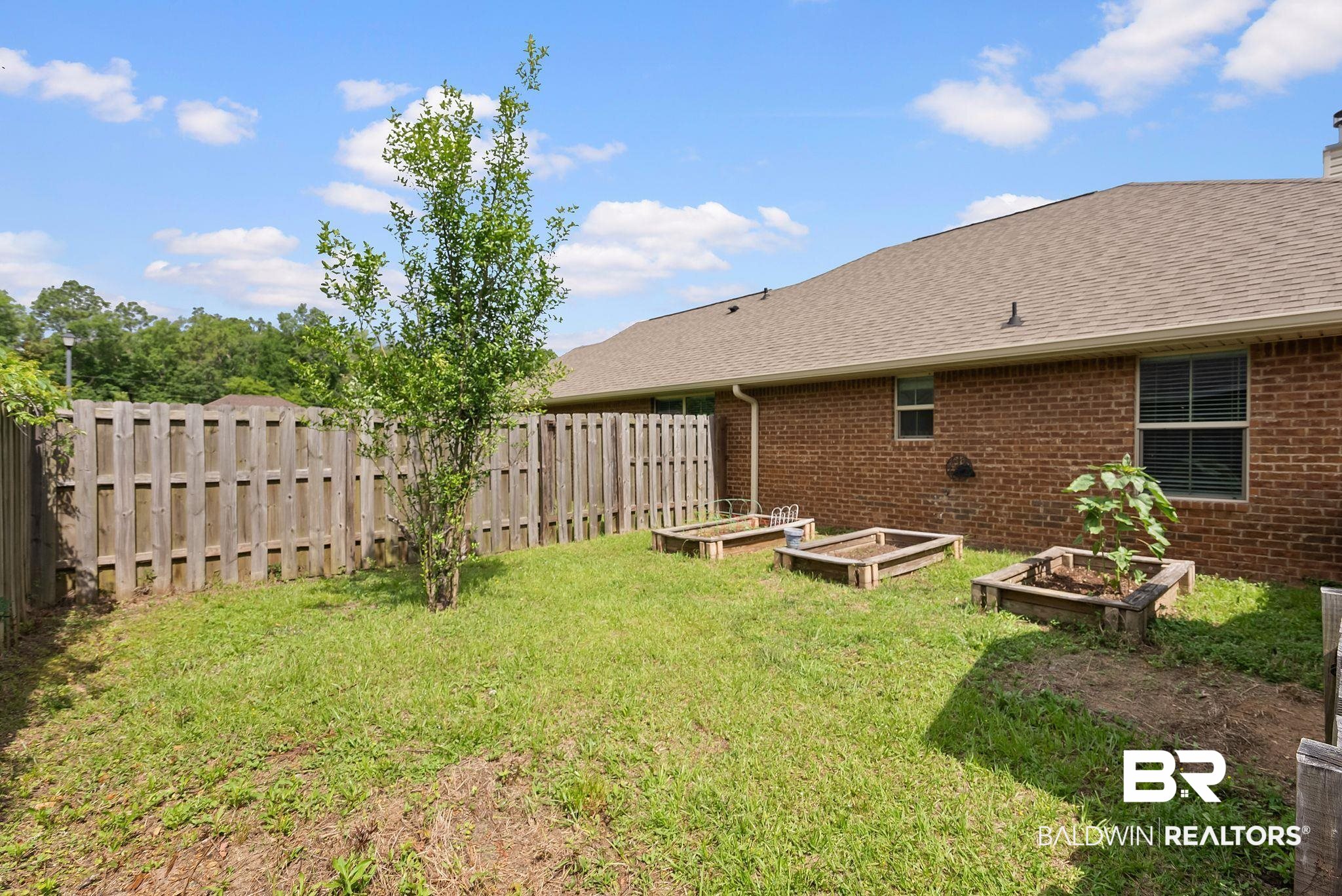 22076 Garland Loop Silverhill, AL 36576 - Photo 23 of 27 Fenced backyard featuring a brick exterior, multiple raised garden beds, a young tree, and a shingle roof