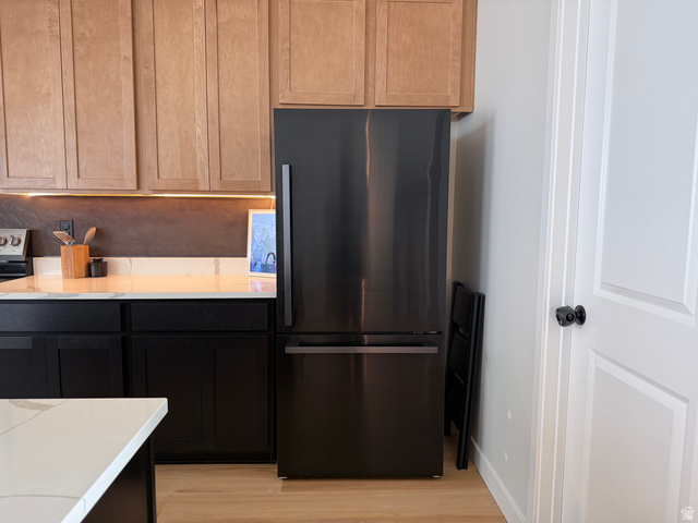 774 West 480 South American Fork, UT 84003 - Photo 15 of 76 Stainless steel refrigerator integrated within a kitchen featuring light wood-finish upper cabinetry, black lower cabinetry, and a white countertop with subtle veining