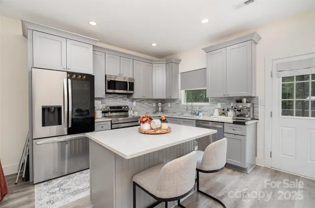 a kitchen with stainless steel appliances granite countertop a stove a sink a microwave a refrigerator and white cabinets