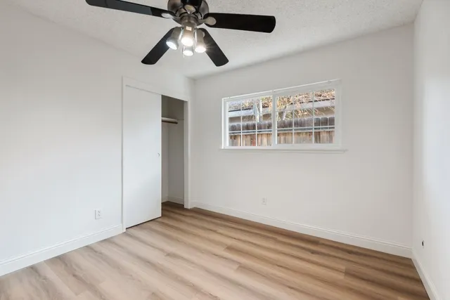 an empty room with wooden floor chandelier fan and windows