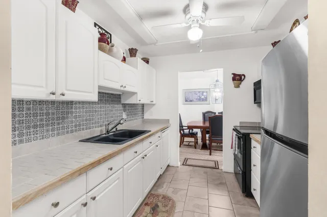 a kitchen with granite countertop a refrigerator a sink dishwasher and white cabinets with wooden floor