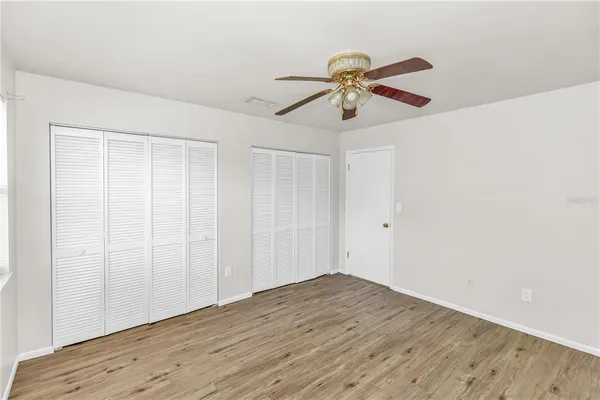 an empty room with wooden floor closet and fan