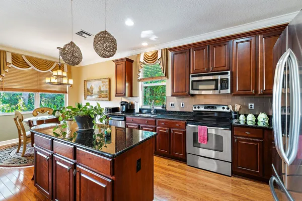 a kitchen with stainless steel appliances granite countertop a refrigerator a stove a sink a dining table and chairs with wooden floor