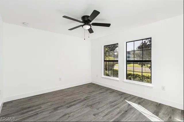 an empty room with wooden floor fan and windows