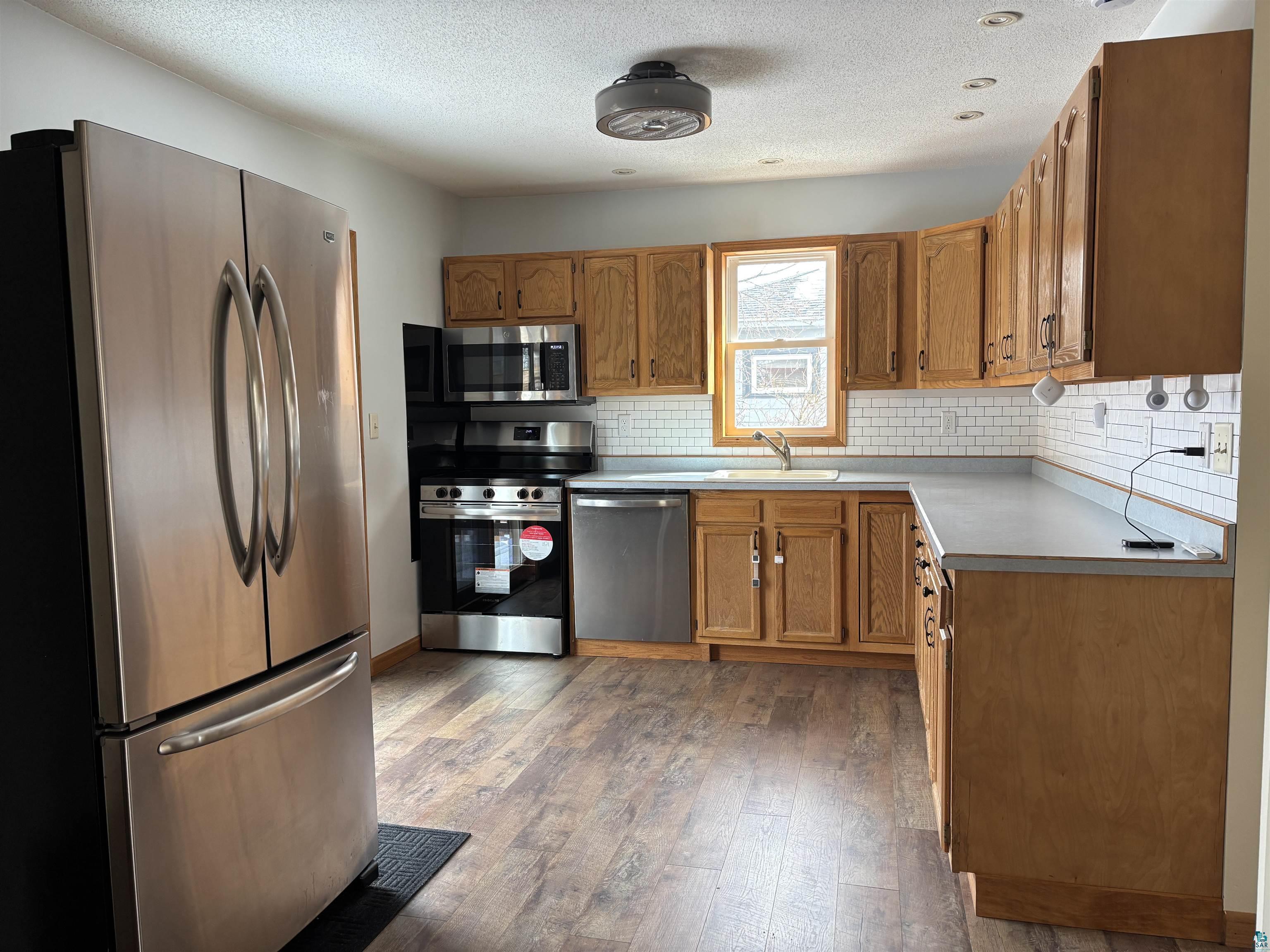 21 4th Street Proctor, MN 55810 - Photo 16 of 35 Kitchen with a sink, light wood finished floors, brown cabinets, stainless steel appliances, and decorative backsplash